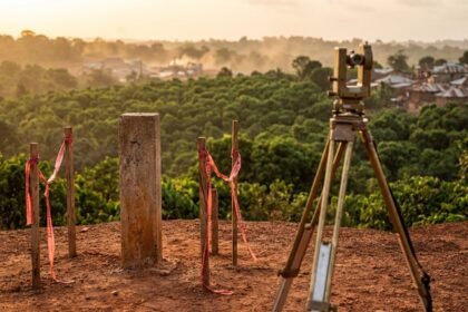 Survey boundary pillar and pegs in red earth, with farms, forest and a distant mining area behind